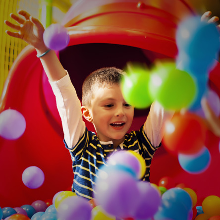 Child in ball pit full of colourful balls throwing them in the air